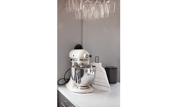 Vit kitchen aid bakmaskin på en vit köksbänk, bredvid står hushållspapper och ovanför hänger vinglas. 