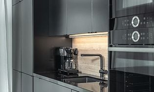 Ett svart kök drar uppmärksamheten till sig, här är ugn, mikro och kylskåp integrerat i samma stil. Även kaffemaskinen är svart.
