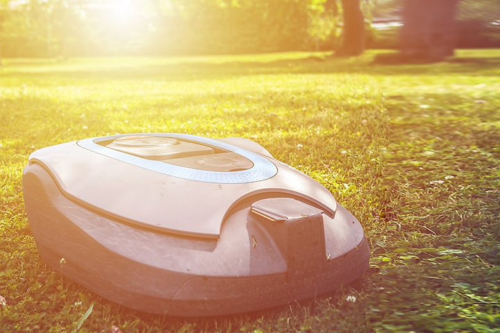 Robotgräsklippare på gräsmatta med en stor sol som skiner i bakgrunden. 