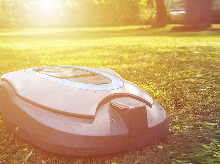 Robotgräsklippare på gräsmatta med en stor sol som skiner i bakgrunden.