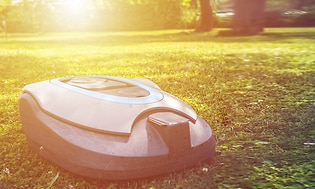 Robotgräsklippare på gräsmatta med en stor sol som skiner i bakgrunden. 