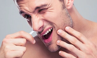 Man som plockar näshår med en pincett och grimaserar. 