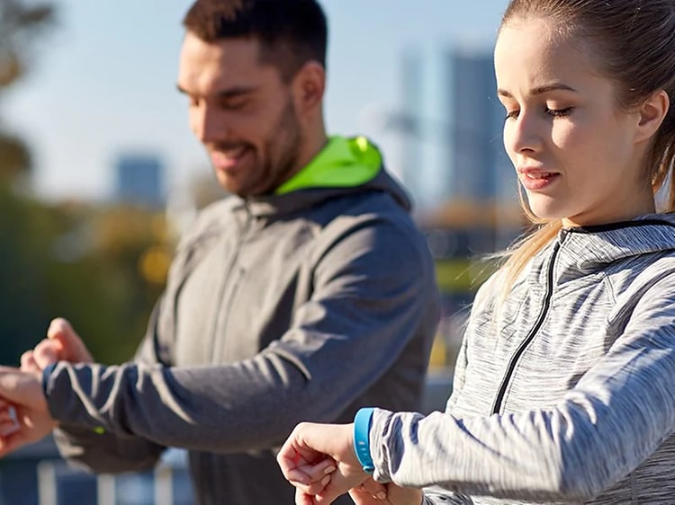 En kvinna och en man i träningskläder justerar sina smartklockor innan de startar på en springtur. 