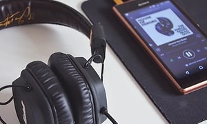 En mobiltelefon som ligger på ett bord och spelar musik via ett svart headset som ligger bredvid. 