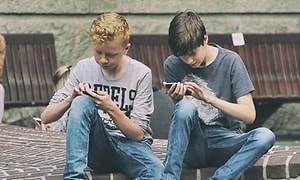 Två unga grabbar i jeans och t-shirt sitter och ser på var sin mobiltelefon. 