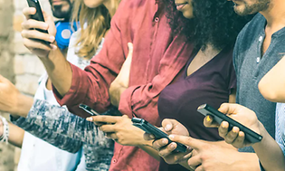 Flera personer står tätt på rad i färgglada kläder och ser på sina mobiltelefoner.