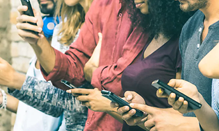 Flera personer står tätt på rad i färgglada kläder och ser på sina mobiltelefoner. 