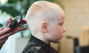 Bild från sidan på en pojke som får håret klippt med en hårklippare. 