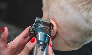Pojke som får håret klippt runt öronen med en hårklipps-apparat av kvinna med röda naglar. 
