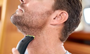 Man rakar halsen med en Philips OneBlade Pro, en liten svart trimmer med illgrönt rakhuvud. 