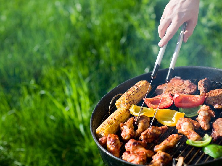 En kolgrill full med kött och grönsaker utomhus.