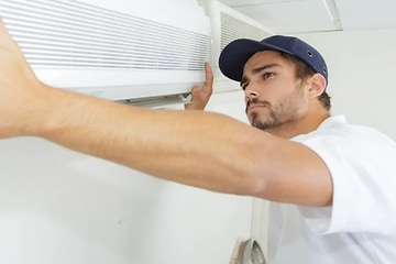 En man placerar en värmepump mot en vägg.