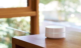 Vit och rund Google WiFi mesh-enhet placerad på ett träbord.