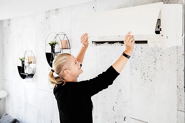 Kvinna öppnar upp locket på en vit värmepump på väggen för att kolla filtret. 