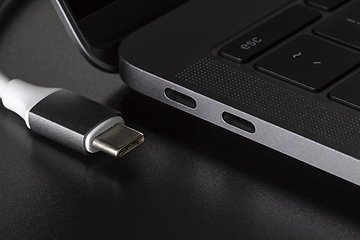 En USB-kabel med vit sladd ligger bredvid en bärbar dator med olika portar på sidan.