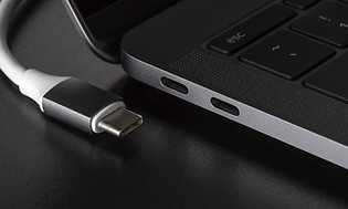 En USB-kabel med vit sladd ligger bredvid en bärbar dator med olika portar på sidan.