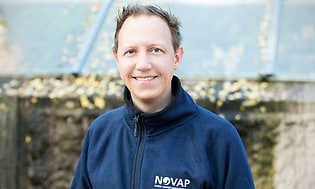 Man ler mot kameran och är klädd i en blå jacka med NOVAP logotyp. 