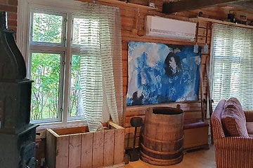 En vit värmepump uppsatt på väggen mittemellan två fönster i en klassisk stuga i trä. 