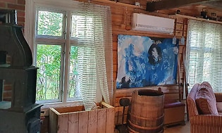 En vit värmepump uppsatt på väggen mittemellan två fönster i en klassisk stuga i trä. 