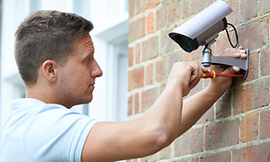 En man installerar övervakningskamera på husvägg