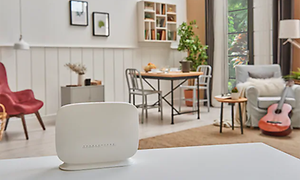 Vi router placerad på en vit bänk i ett stort rum med ett litet köksbord, två fåtöljer och en gitarr bland annat.