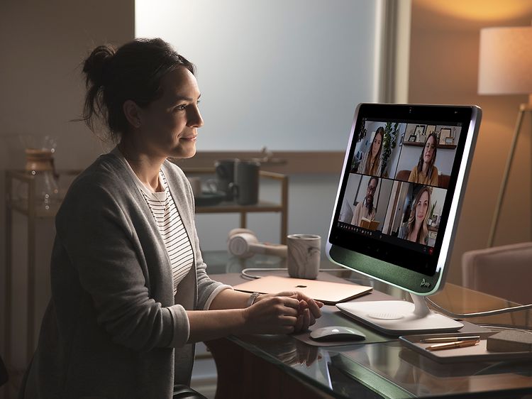 Kvinna sitter vid ett skrivbord och har videomöte med fyra andra personer på en stor skärm. 