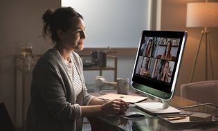 Kvinna sitter vid ett skrivbord och har videomöte med fyra andra personer på en stor skärm. 