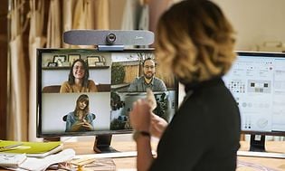 Kvinna med ryggen till ser på en skärm med fyra andra personer som deltar i ett videomöte. 