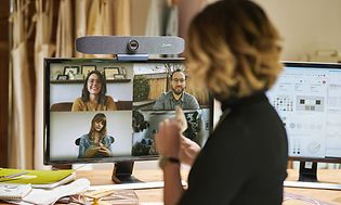 Kvinna med ryggen till ser på en skärm med fyra andra personer som deltar i ett videomöte.