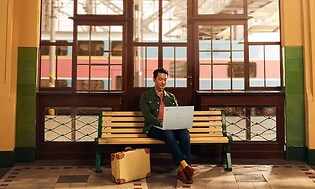Man med bärbar dator som sitter på en bänk på en tågstation