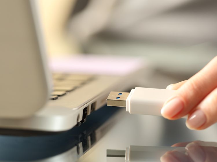 Närbild på en hand som ansluter ett vitt USB-minne till en bärbar dator.