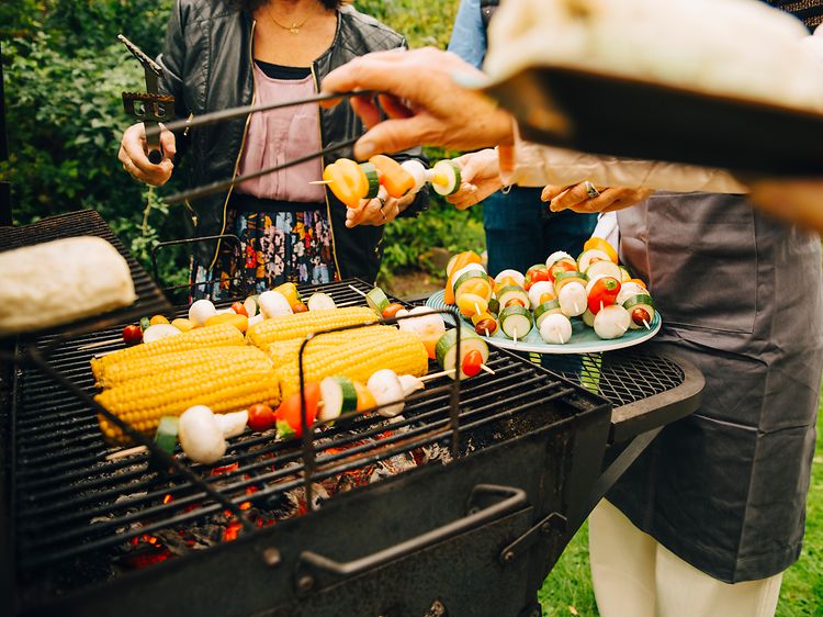 Människor som står runt en kolgrill som grillar grönsaker