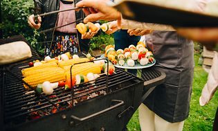 Människor som står runt en kolgrill som grillar grönsaker