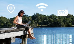 Kvinna som sitter på en brygga vid en sjö och arbetar på en bärbar dator
