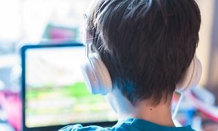 Gaming - Pojke med hörlurar sitter framför bärbar dator och gamear.
