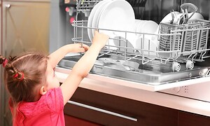 En liten flicka framför en öppen diskmaskin som är full med disk.