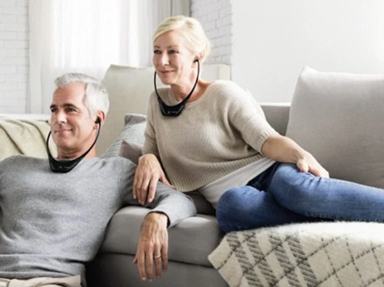 Man och kvinna sitter i en soffa och ser på TV med trådlösa hörlurar på sig.