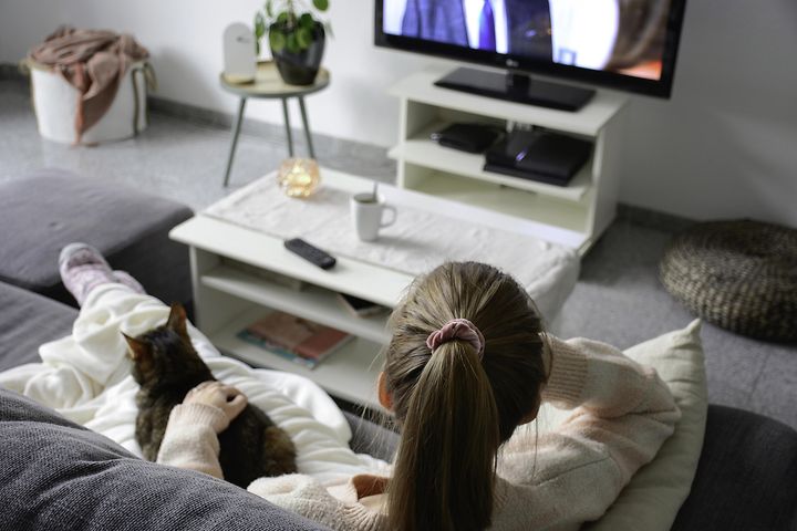 Kvinna sitter med en katt i en soffa och ser på TV.