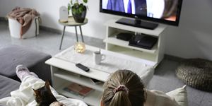 Kvinna sitter med en katt i en soffa och ser på TV.