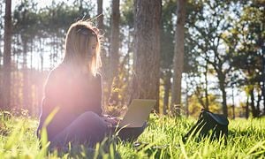Kvinna sitter i gräset och jobbar på en laptop