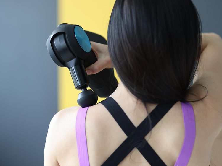Kvinna som står med ryggen mot oss och använder en massagepistol