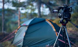 Kamera på stativ i en skog som pekar mot ett tält