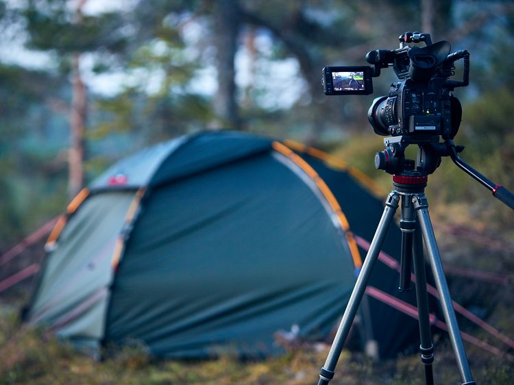 Kamera på stativ i en skog som pekar mot ett tält