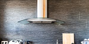 Kitchen fan haning over the stove, with differnt kitchen utitilies beside the stove