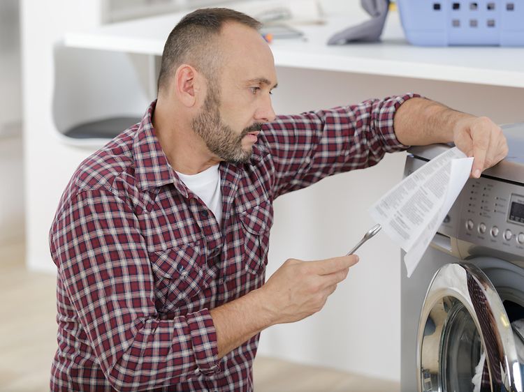 En man som kontrollerar instruktionerna när han monterar tvättmaskinen