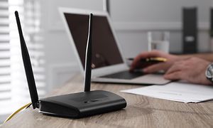 Router bredvid en bärbar dator på ett skrivbord och händer på tangentbordet.