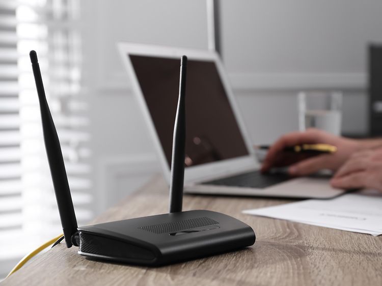 Router bredvid en bärbar dator på ett skrivbord och händer på tangentbordet.