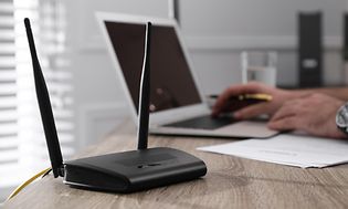 Router bredvid en bärbar dator på ett skrivbord och händer på tangentbordet.