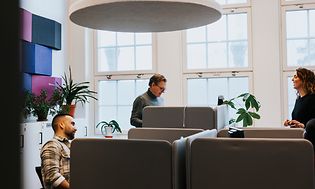 Två män och en kvinna vid deras skrivbord på ett kontor