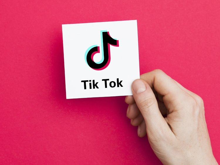 En hand håller i ett vitt kort med TikTok logga på, mörkrosa bakgrund.